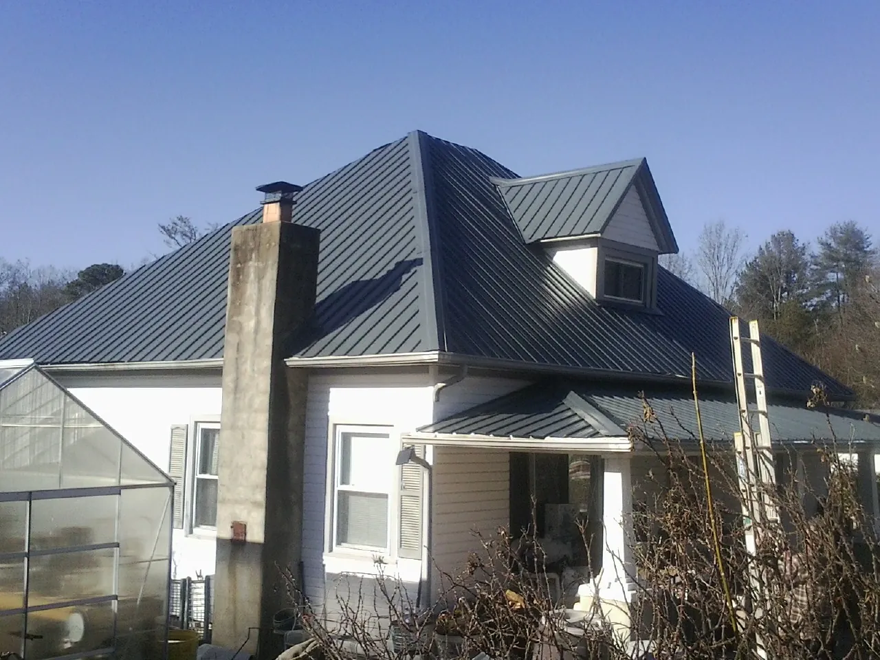 Dark blue standing seam metal roof on a white farmhouse with dormer — Slate & Tile Roof Repair by Roofing Brothers in Tropic