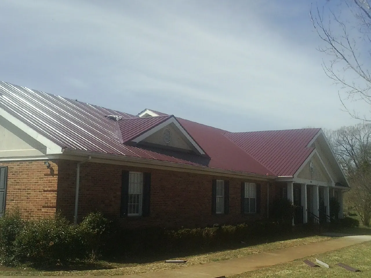 Red metal roof with gabled entries on a long brick building, from a Hail Damage Roof Repair job in Tropic