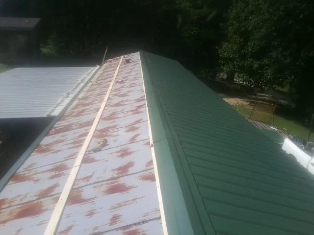 Old rusted panels beside newly installed green metal roofing — Wind Damage Roof Repair by Roofing Brothers in Tropic