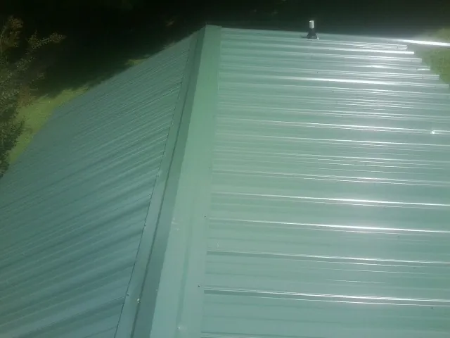 New green metal panels meeting at the ridge of a roof — Flat Roof Repair work by our crew in Tropic