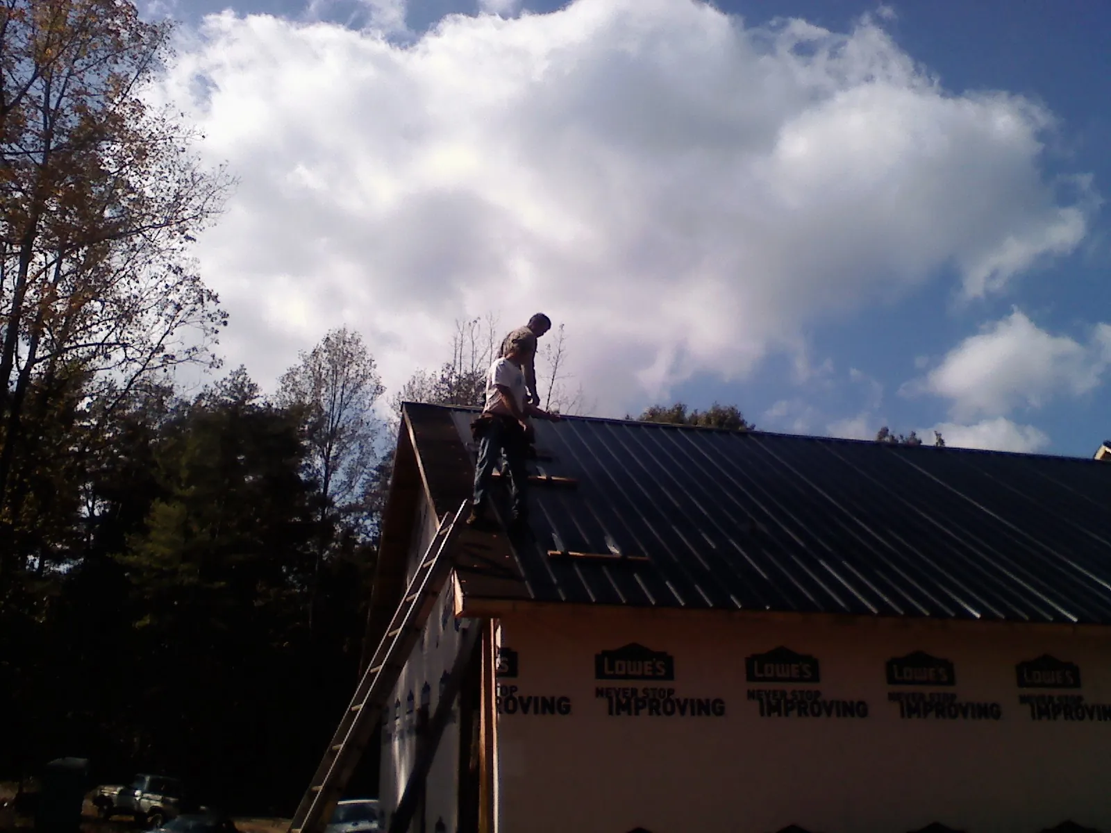 Roofer fastening dark metal panels high against a cloudy sky, from a Roof Inspection job in Tropic