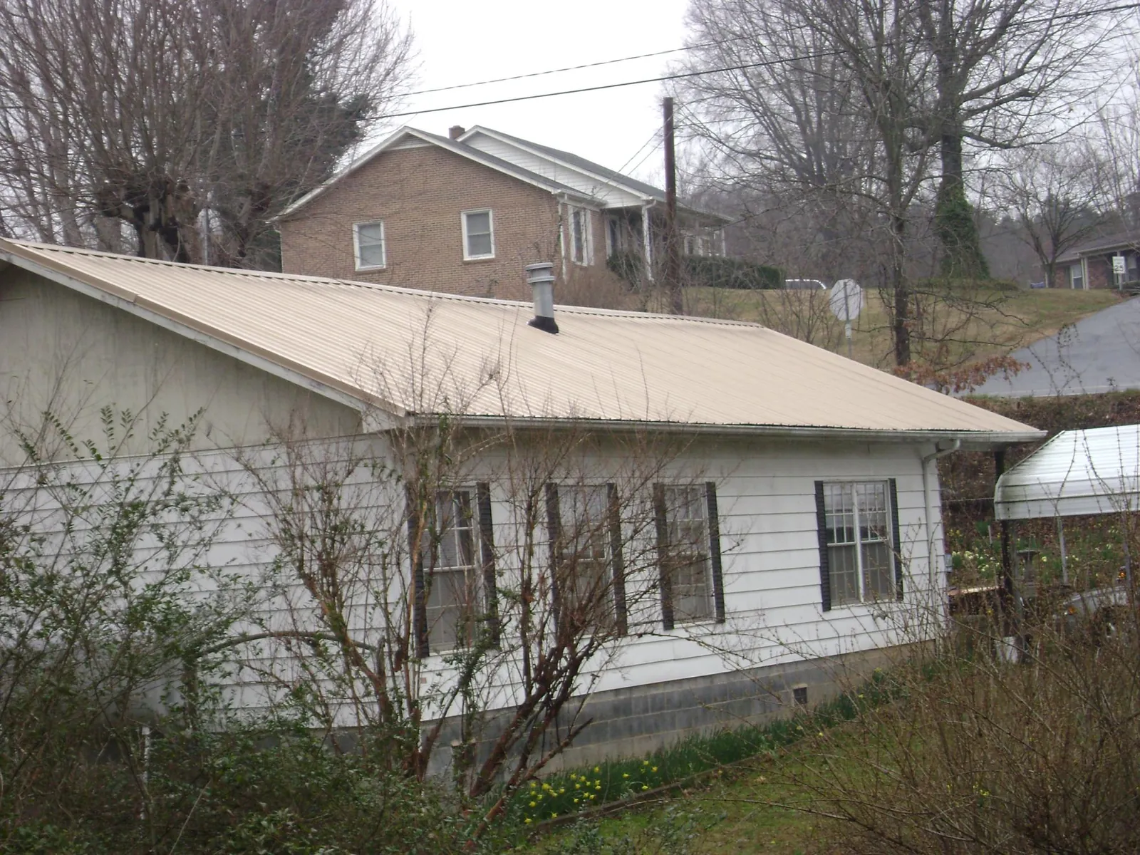 Tan metal roof on a white sided house set into a hillside — Commercial Roofing by Roofing Brothers in Tropic