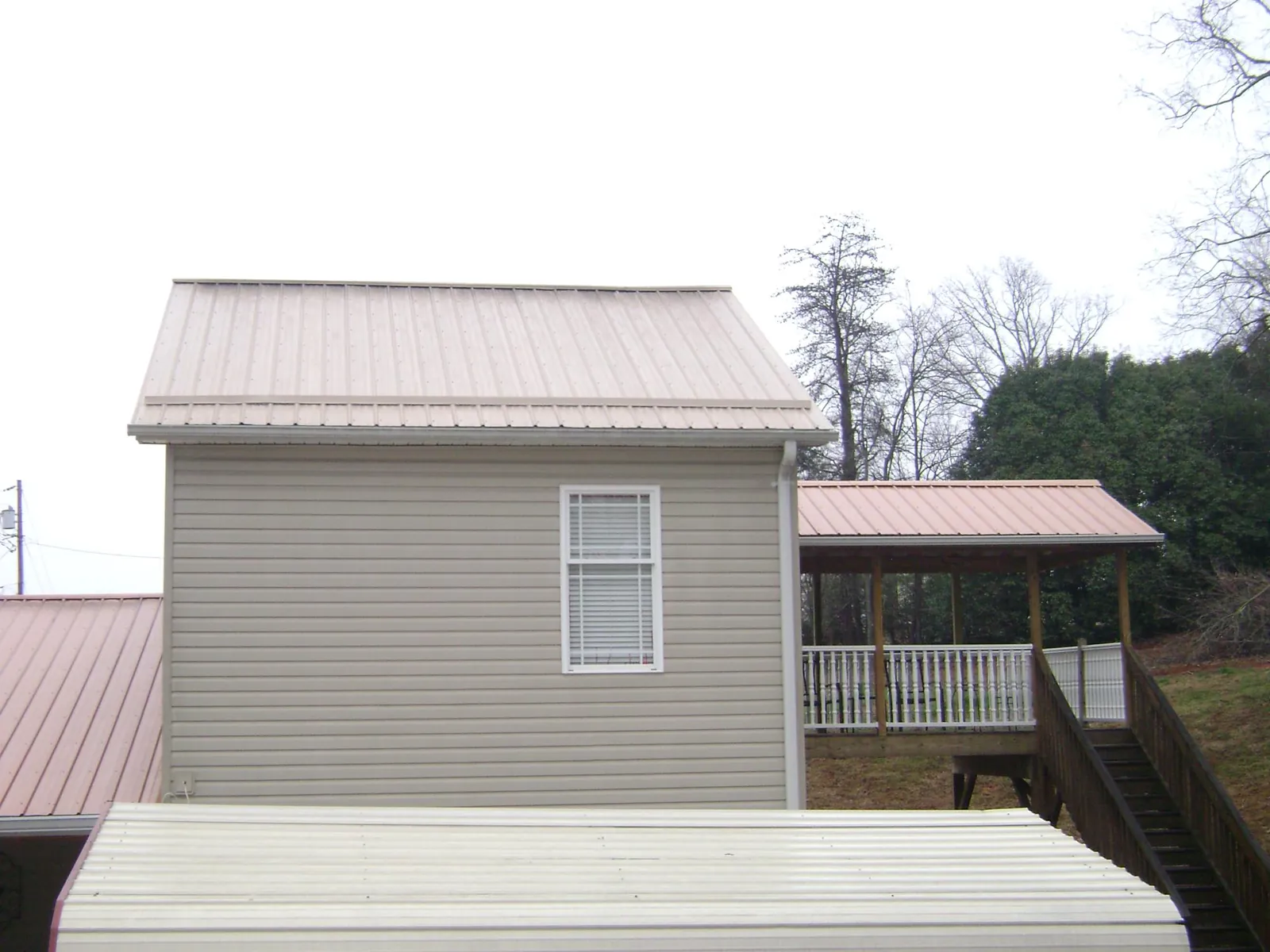 Tan metal roofs on a two story addition and attached porch, from a Roof Replacement job in Tropic